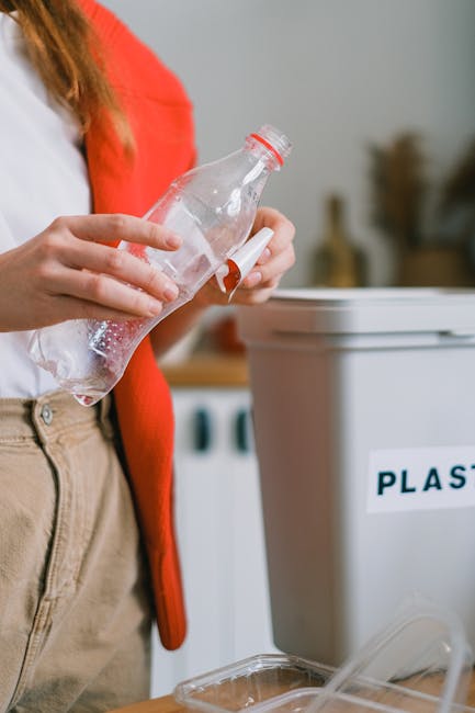 A person dressed in orange work overalls is standing inside a property, holding two large blue plastic garbage bags filled with items, one in each hand, during a home relocation process. The person is